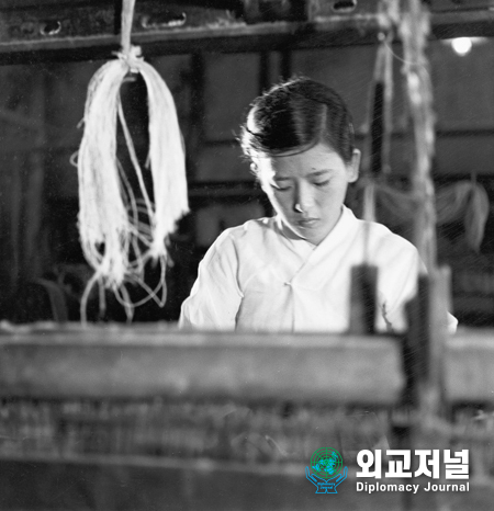  한국에서의 산업<br>
20살인 황영옥은 부산의 조선 직물 회사의 코튼 룸에서 일한다.<br>
2주일에 한번 쉬며 하루에 17시간 일하고, 한달에 $15에 상당하는 급여를 받는다.<br>
1950년 9월 한국 부산<br>
<br>
INDUSTRY IN KOREA<br>
Whang Yung Ok, 20 years of age, works on a cotton loom in the Chosen Textile<br>
Company in Pusan. She is paid the equivalent of $15.00per month for an eleven-hour<br>
working day with one off every two weeks.<br>
South Korea. September 1950