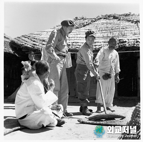  한국 생활<br>
유엔 사진 기자 그렌트 맥린과 통역자 박현리는 부산 근처 감촌리 마을에 있다.<br>
그들은 한 농민으로부터 쌀 수확 후 밀을 심을 때 밀알을 말리는 방법을 배우고 있다.<br>
<br>
LIFE IN KOREA<br>
U.N. Photographer GRANT MCLEAN (in beret) and his interpreter HENRY PAK are seen in the village of Kamjyun-ri near Pusan. They are learning how a farmer lays out his wheat grains to dry before planting them after the rice harvest.<br>
South Korea. September 1950.