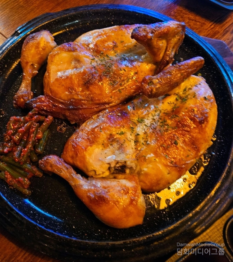 사진은 구도로통닭의 대표 메뉴인 바삭한 통닭구이가 상에 올려진 모습이다. 노릇하게 구워진 닭은 겉은 바삭하고 속은 촉촉하게 익어 군침을 자극한다. 접시 한편에는 매콤하게 무친 밑반찬 나물이 곁들여져, 기름진 맛을 잡아주며 조화를 이루고 있다. 갓 구워낸 통닭의 윤기와 황금빛 바삭함은 시원한 생맥주와 함께 곁들이기 최적이며, 보는 것만으로도 ‘힐링 치맥’을 연상케 한다.