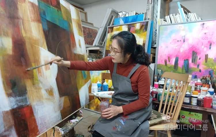 류일지 작가가 작업실에서 ‘축제–유희’ 시리즈 신작을 제작하고 있는 모습. 따뜻한 색감과 감성적 추상을 특징으로 하는 작가의 작품 세계는 자연과 인간의 조화, 그리고 삶의 유희를 회화적으로 표현한다. (사진제공 = 류일지 작가)